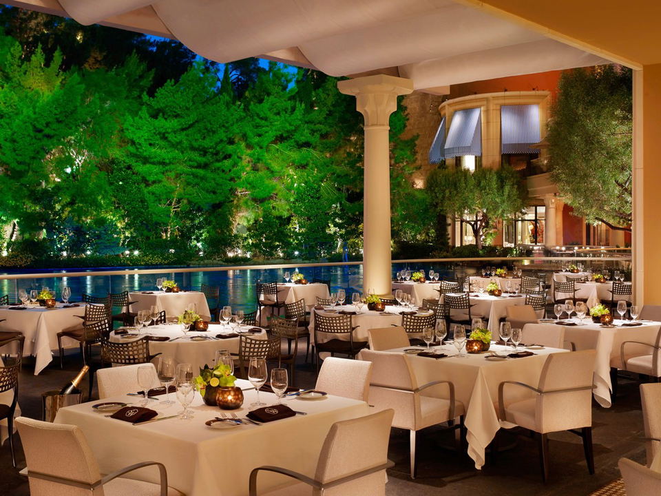 An upscale outdoor patio dining room at SW Steakhouse at Wynn Las Vegas, featuring white-tablecloth tables set with wine glasses and candles, warm