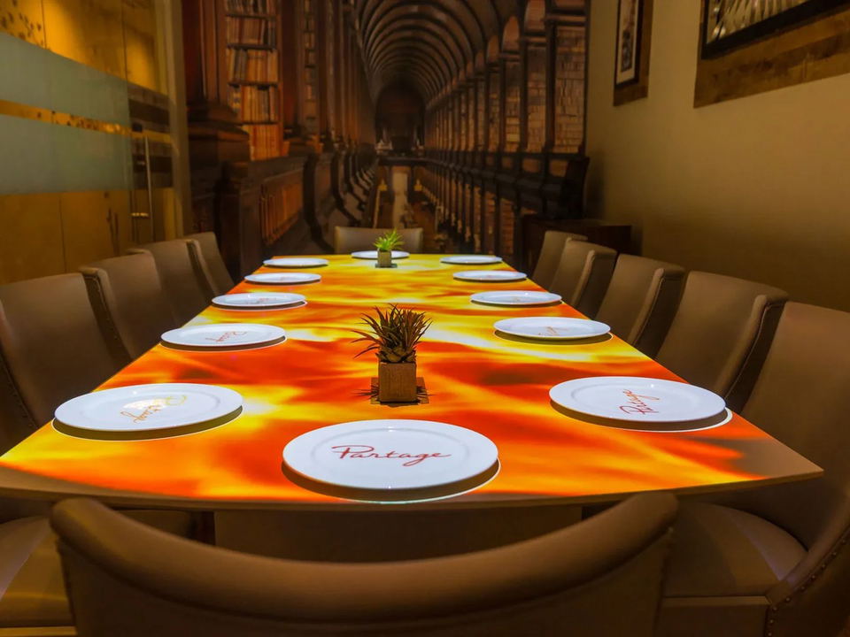 A long private dining table at Partage Las Vegas with a projected orange and yellow light display, set with white plates and small plant