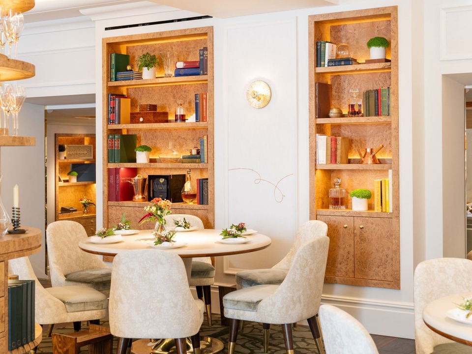 An elegant dining room with cream chairs around a round table, flanked by burl-wood bookshelves with amber backlighting.
