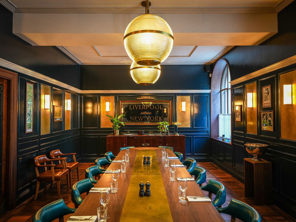 A private dining room with dark paneled walls, a long wooden table set with teal leather chairs, and two large globe pendant lights.
