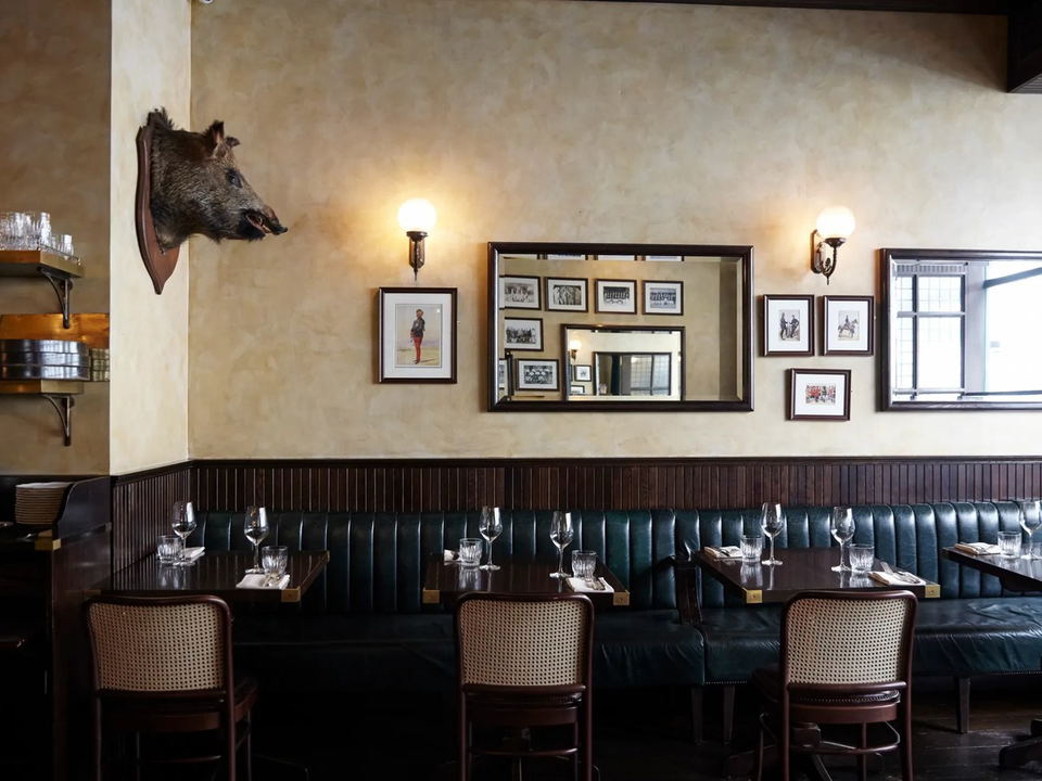 Interior of a restaurant with green banquettes, framed artwork, and a boar's head.