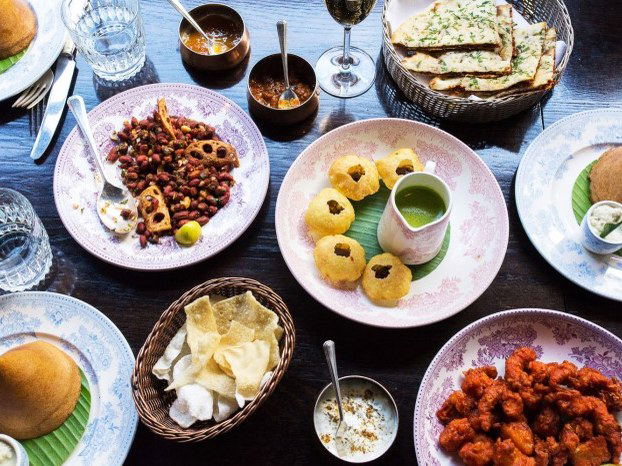 An overhead shot of a spread of Indian dishes, including pani puri, a bean dish, fried items with chutney, papadums, and naan.