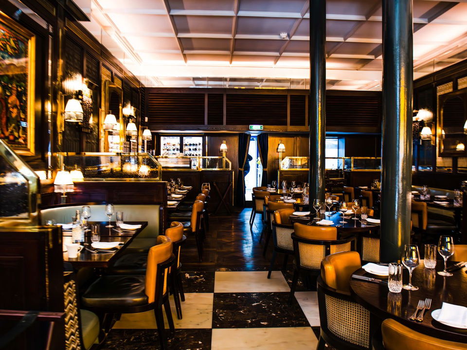 An upscale restaurant interior with dark wood paneling, leather and cane chairs, and a black-and-white marble floor.