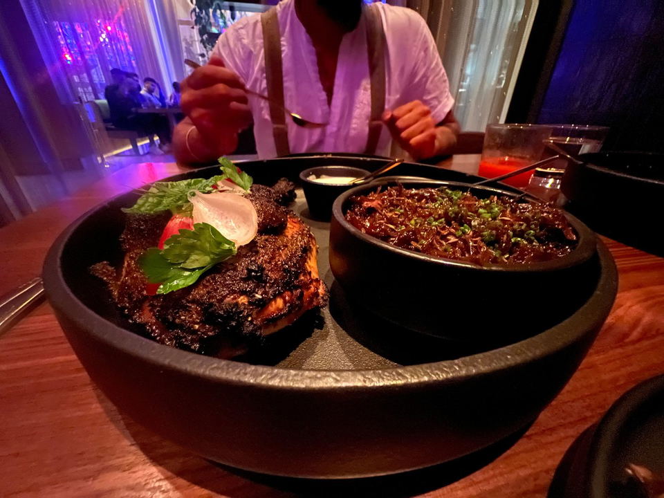 Tatiana by Kwame Onwuachi: Charred meat and a braised dish served in a dimly lit restaurant setting.