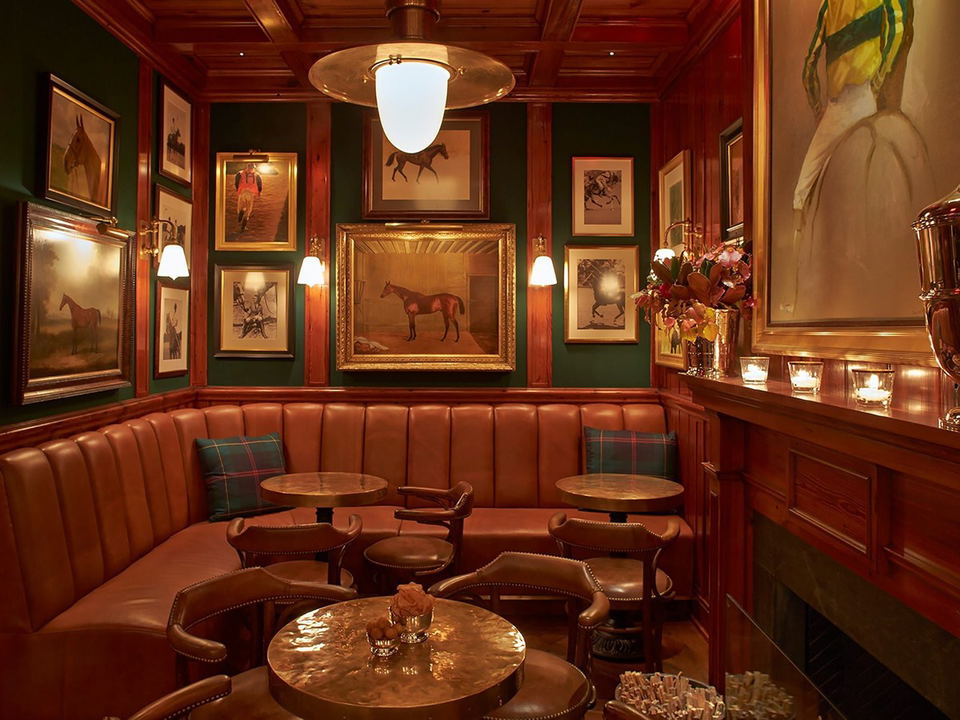 The clubroom at Ralph Lauren's Polo Bar, with dark green walls, mahogany paneling, leather banquette seating, equestrian artwork, and brass lighting.