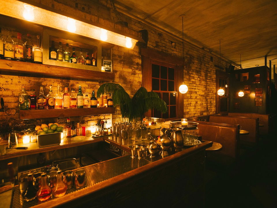 An intimate walk-in cocktail bar offers a warmly lit interior with exposed brick and a well-stocked bar.