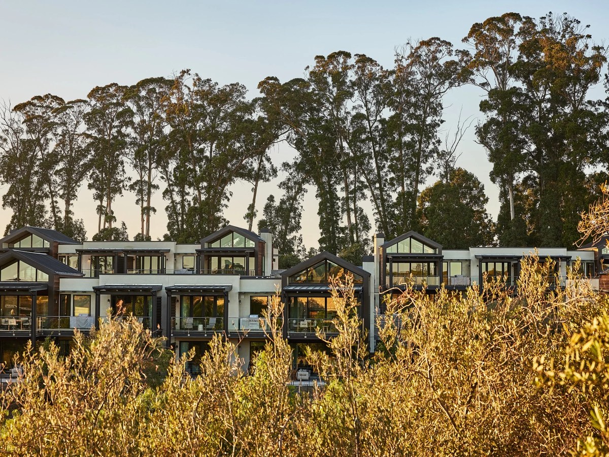 Modern multi-unit luxury resort accommodations with dark-framed gabled roofs and large glass windows, nestled among tall eucalyptus trees.