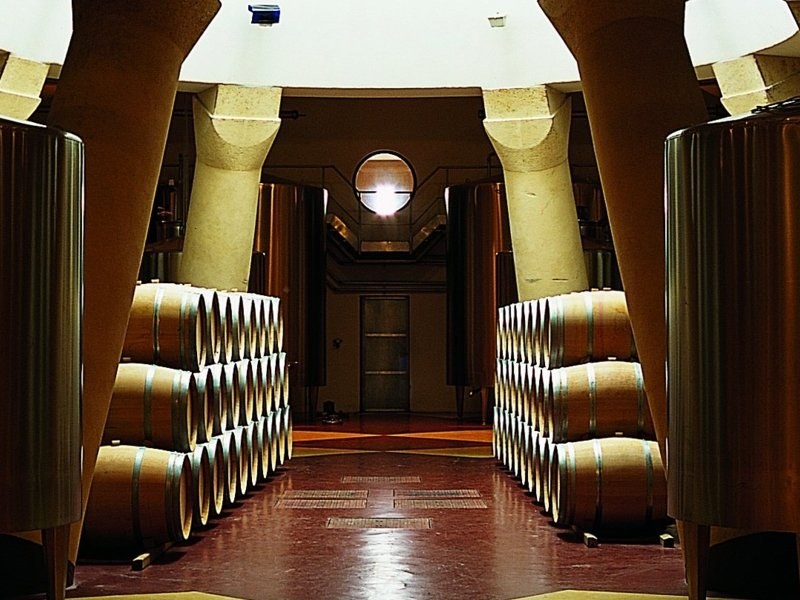 Château Pichon Baron's barrel cellar with rows of oak barrels and fermentation tanks under vaulted arches.