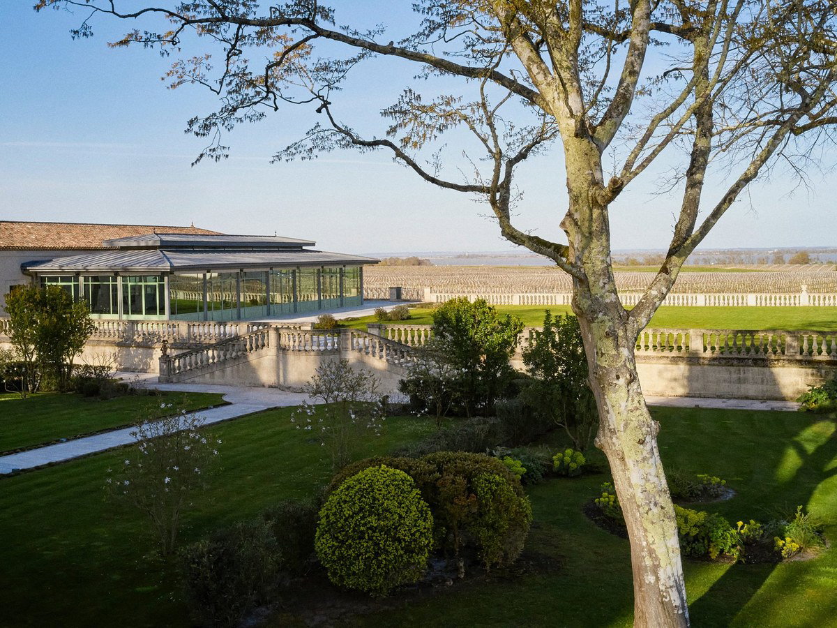 An elevated view of Château Pichon Longueville Comtesse de Lalande, showing its formal gardens, a modern glass pavilion, and vineyards.