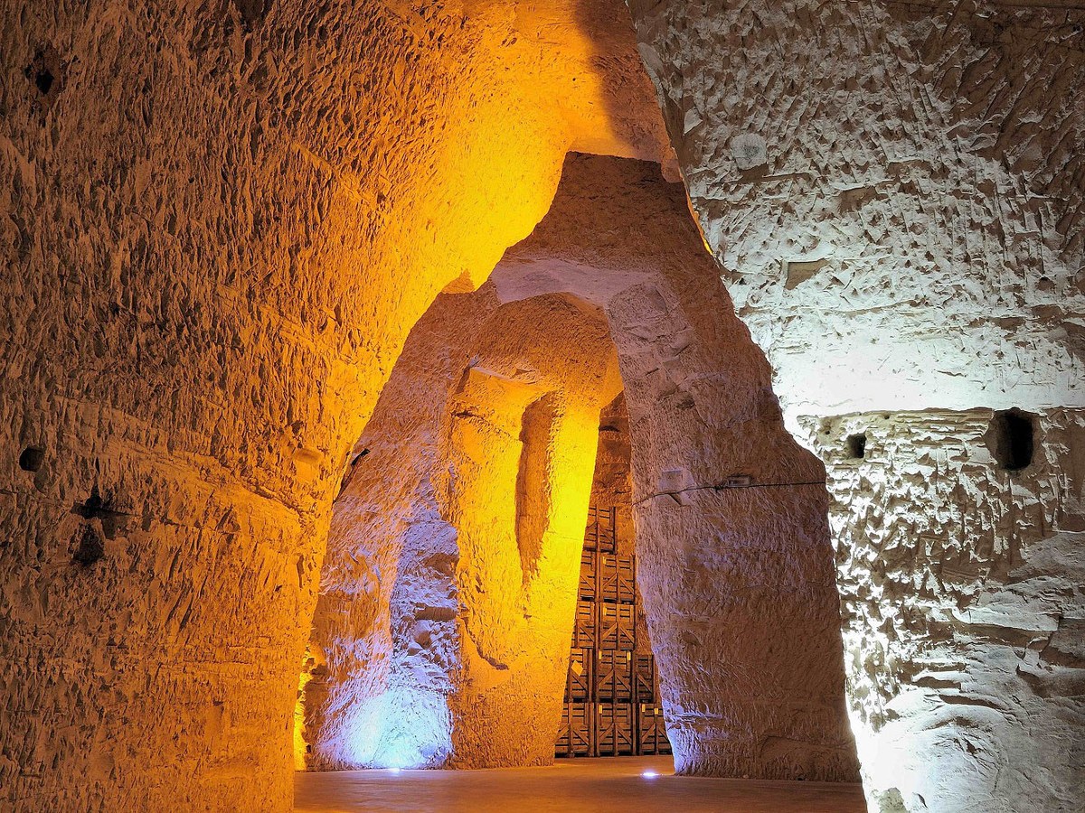 Dramatic wide-angle shot of vast Gallo-Roman chalk tunnels with vaulted ceilings and raw chalk walls, illuminated by golden uplighting.