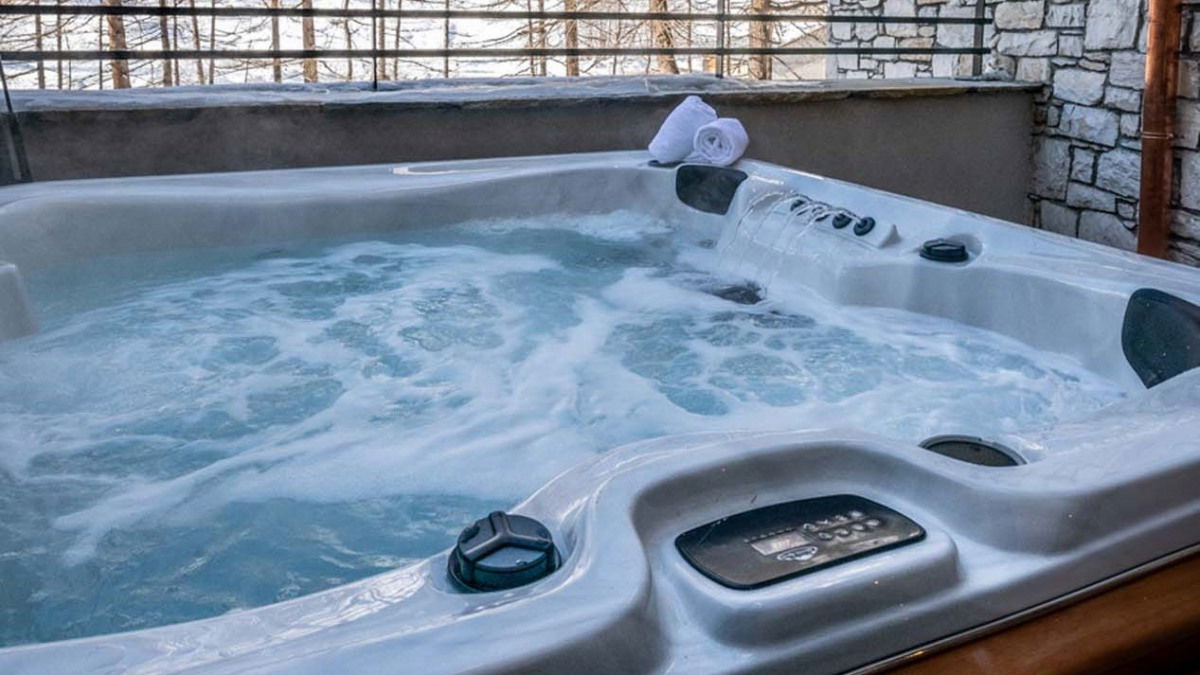An outdoor hot tub with bubbling water on a covered terrace, overlooking a snowy winter landscape with trees.
