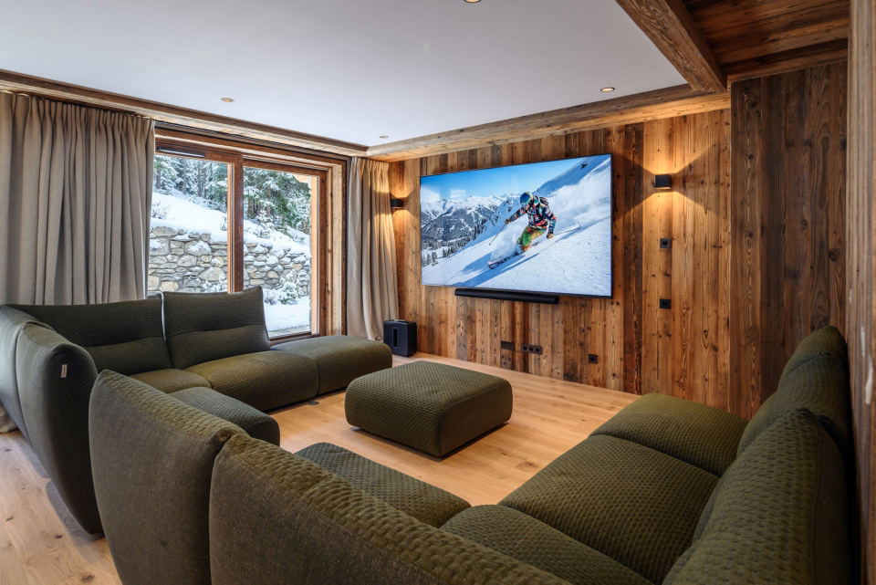 A cozy media room at chalet pierre méribel, featuring wood-paneled walls and an olive-green modular sofa.