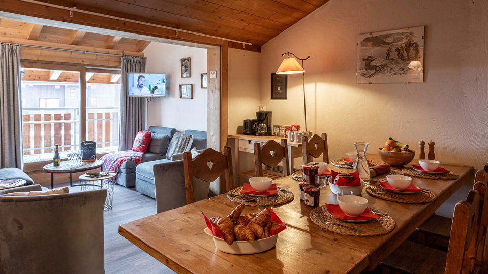 Chalet Pierre Méribel offers a cozy breakfast setup with fresh croissants and red place settings on a rustic wooden table.