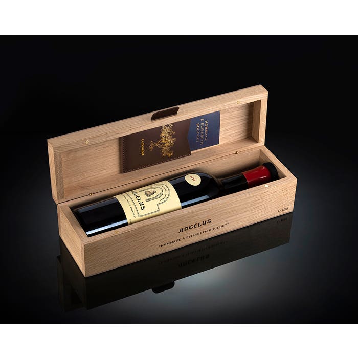 An open wooden wine box displaying a bottle of Château Angelus wine with label visible, along with papers and a red item inside the natural wood case.