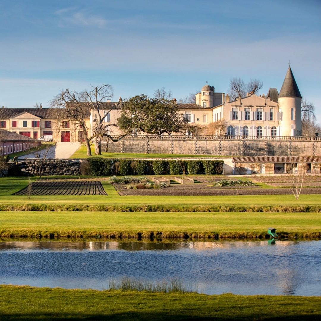 The turreted chateau and walled estate of Chateau Lafite Rothschild in Pauillac, Bordeaux, reflected in a foreground pond.