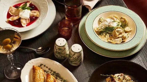 An overhead shot of an intimate tasting menu spread with multiple plated courses, wine glasses, and decorative elements on a dark wood table.