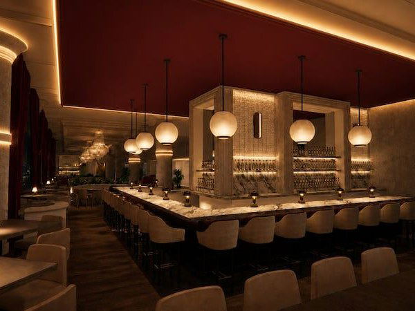 The Carlyle Club offers a warmly lit, upscale bar interior with a long marble-topped bar and globe pendant lights.