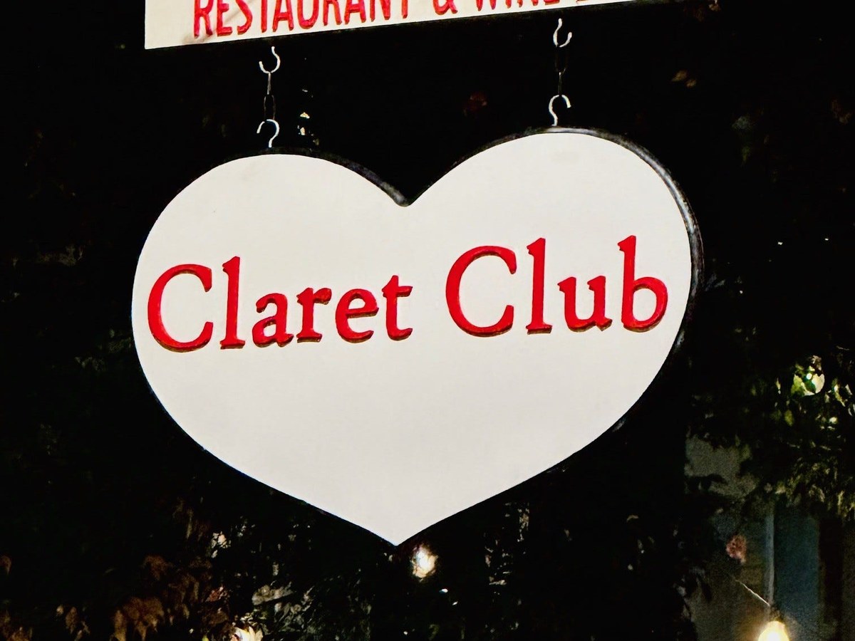 A heart-shaped hanging sign reading 'Claret Club' with a banner above reading 'Restaurant & Wine Bar', photographed at night with string lights.