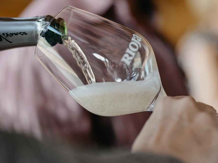 Sparkling Espumoso de Calidad de Rioja DOCa wine is poured from a green bottle into a tilted glass, creating a foamy head.