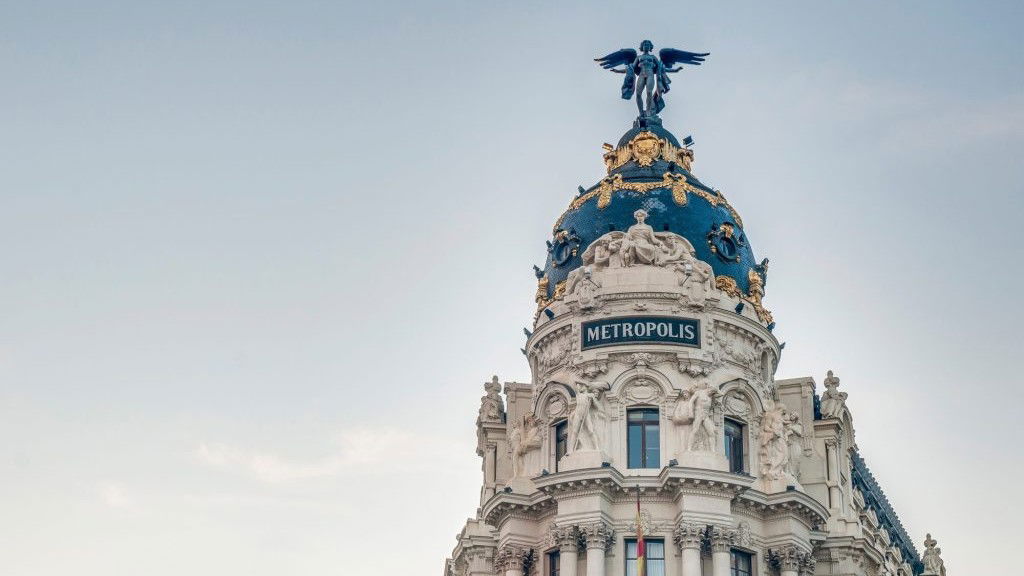 The ornate dome and upper facade of the Metrópolis Building in Madrid, with a statue on top and 'METROPOLIS' signage.
