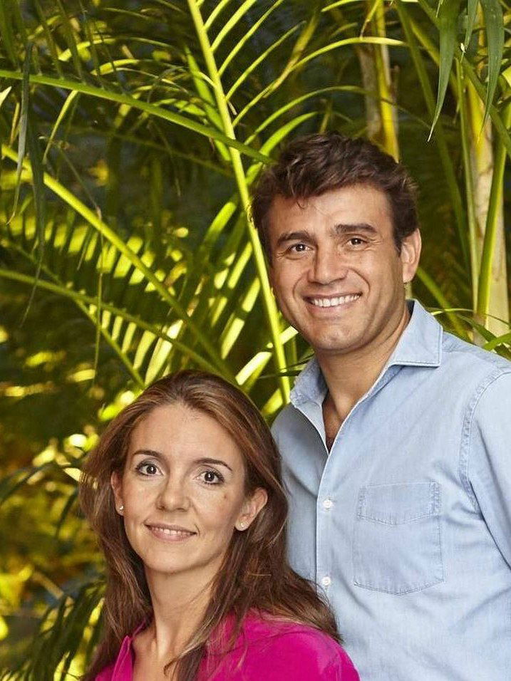 A professional portrait shows Marta Seco in a bright pink blouse, seated, and Sandro Silva in a light blue shirt, standing, against a backdrop of
