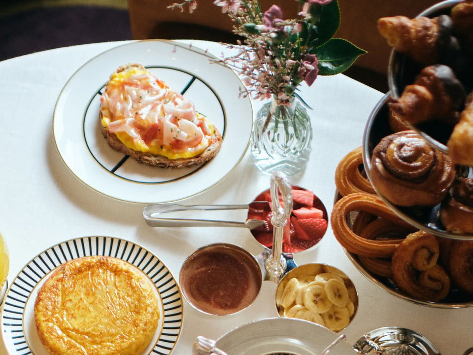 An overhead shot of an elegant breakfast or brunch table setting with pastries, a savory toast, juice, and flowers.