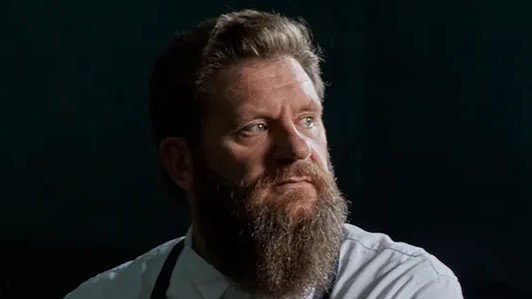 Michael Cimarusti, a bearded chef, in a white shirt and dark apron, seated at a table.