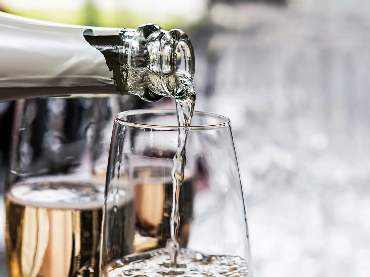 Sparkling wine is poured into a glass, with other filled glasses visible in the background.