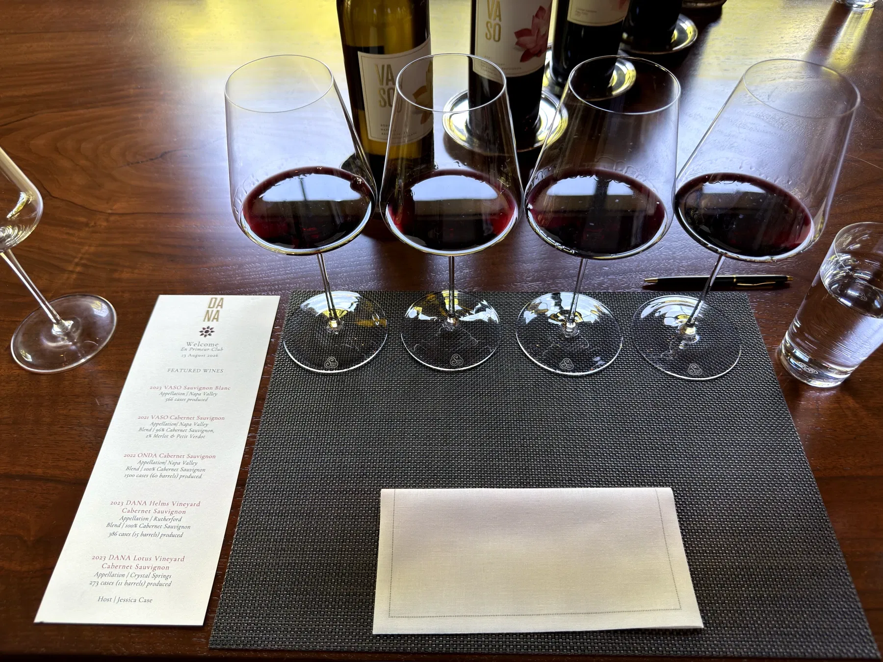 Four red-wine glasses beside the printed En Primeur Club Dana Estates tasting menu dated August 13, 2026