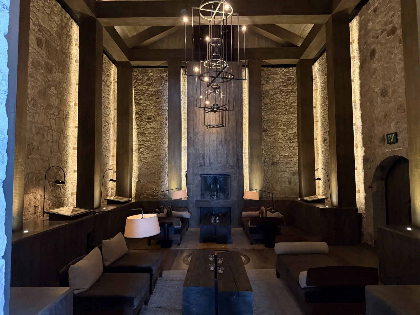 Tall stone salon with timber beams, sculptural chandeliers and fireplace at Dana Estates