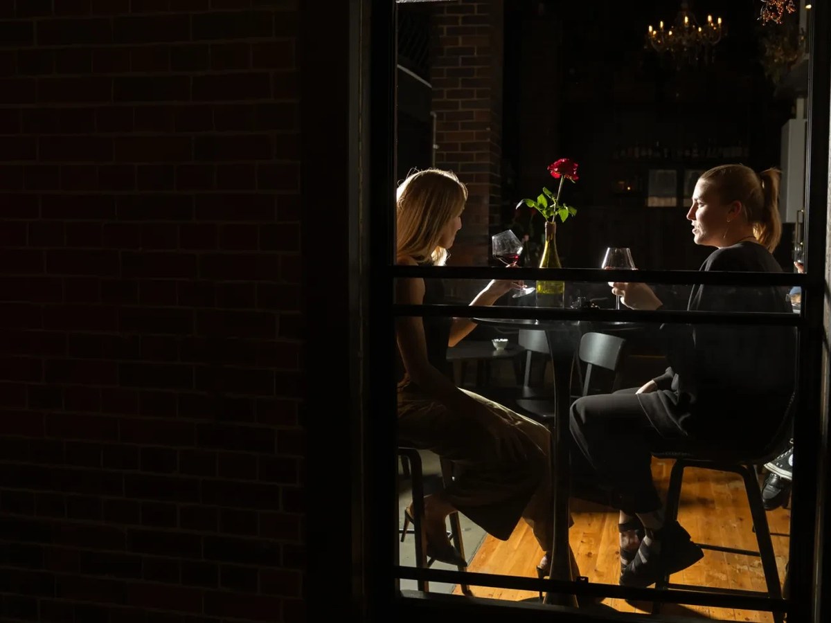 Two women enjoy wine at a table with a flower vase.