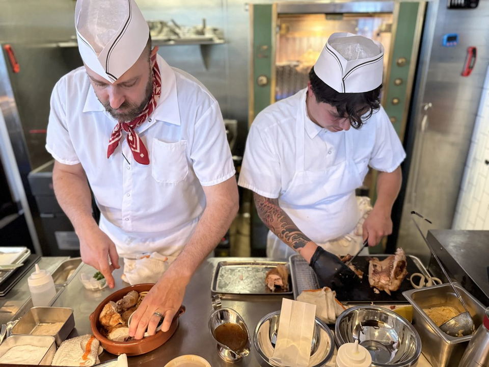 Heretík chefs prepare roasted chicken and other dishes in their kitchen.