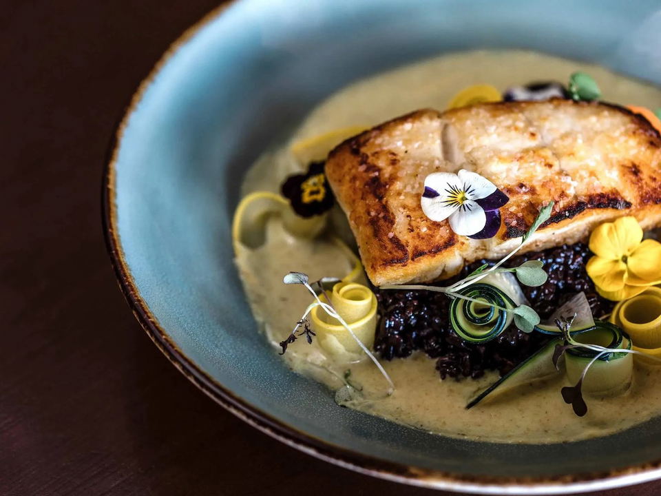 Madeline (Sixth Avenue): A beautifully plated pan-seared fish fillet with edible flowers, zucchini, and microgreens.