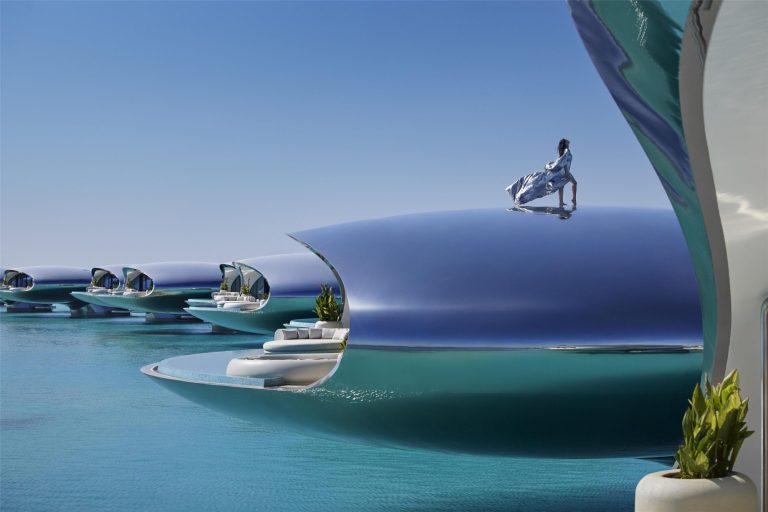 Futuristic luxury resort architecture with curved white and blue structures overlooking turquoise water, featuring floating platforms and modern sculp