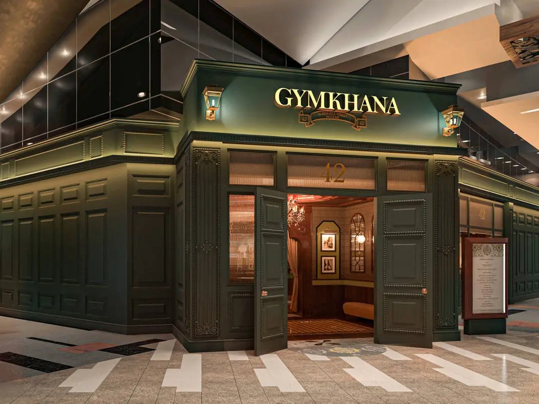 A restaurant storefront with dark green paneled walls, gold lettering reading GYMKHANA above the entrance, and warm lighting visible through the doorway.