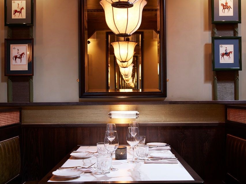 An intimate restaurant dining booth with white tablecloth, crystal glassware, dark wood paneling, and warm lighting; the source page explicitly names 