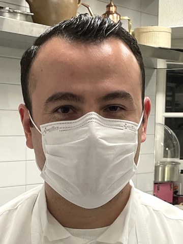 Portrait of a chef in white uniform wearing a face mask in a professional kitchen; source page explicitly identifies this as Executive Chef-Owner Val