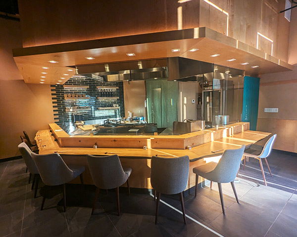 An elegant omakase sushi counter with warm wood surfaces, recessed lighting, and an open kitchen behind glass at Miura Beverly Hills.