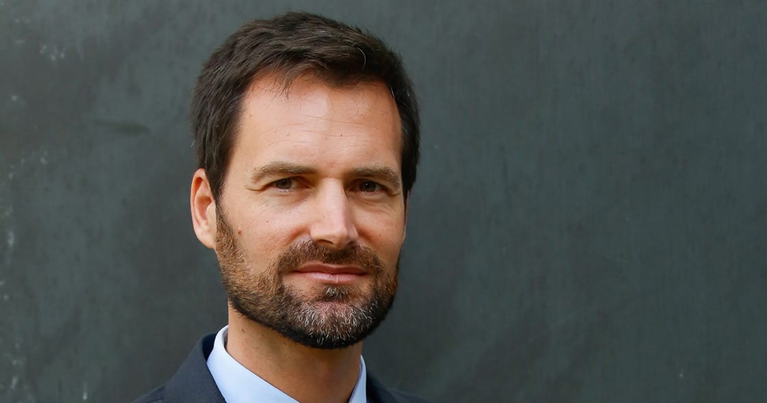 Headshot of Gwendal Poullennec, International Director of the MICHELIN Guides, in a dark suit jacket and light blue shirt against a gray wall.