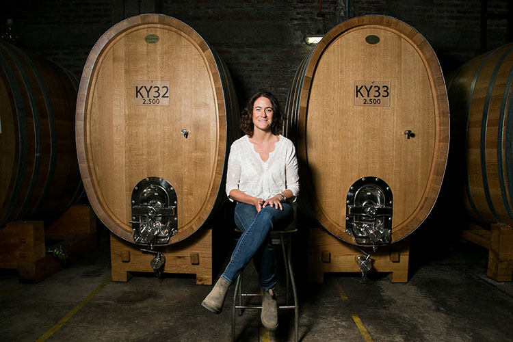 Emily Faulconer among large oak fermentation vessels, reflecting her role at Iconic Wineries of British Columbia.