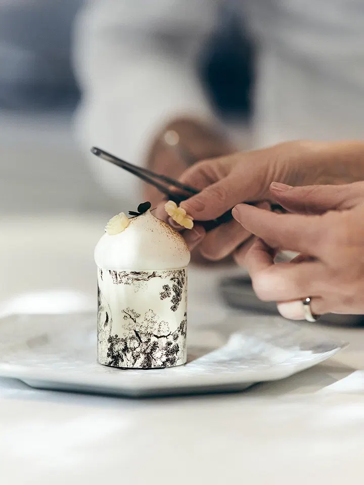 café dior by anne-sophie pic: A chef meticulously garnishes a couture-inspired dessert with delicate flowers.