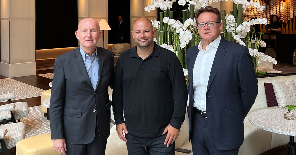 Three men, including Nobu Hospitality CEO Trevor Horwell, pose in an upscale hotel lobby with white orchids and modern decor.