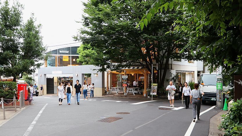 A street scene in Daikanyama, Tokyo, with pedestrians walking past a modern building featuring a "BoConcept" sign and an outdoor cafe.
