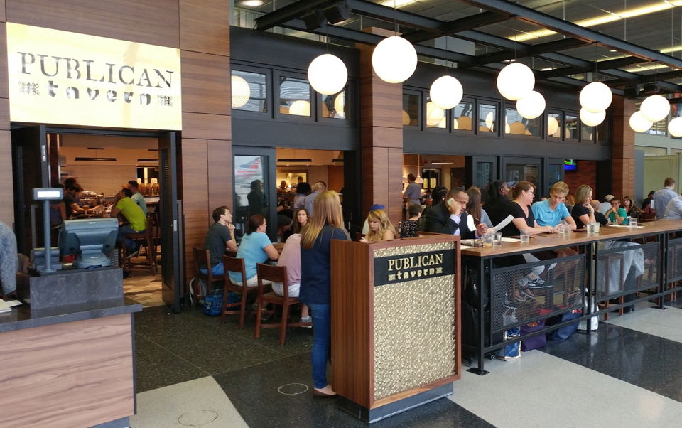 The interior of Publican Tavern at O'Hare Terminal 3, showing patrons dining at tables and a bar, with the 'PUBLICAN tavern' sign visible.