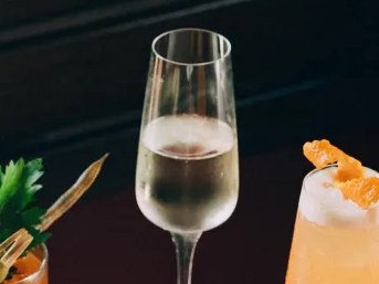 Two cocktails in different glassware, one champagne flute with clear liquid and one rocks glass with a creamy drink garnished with dried fruit.
