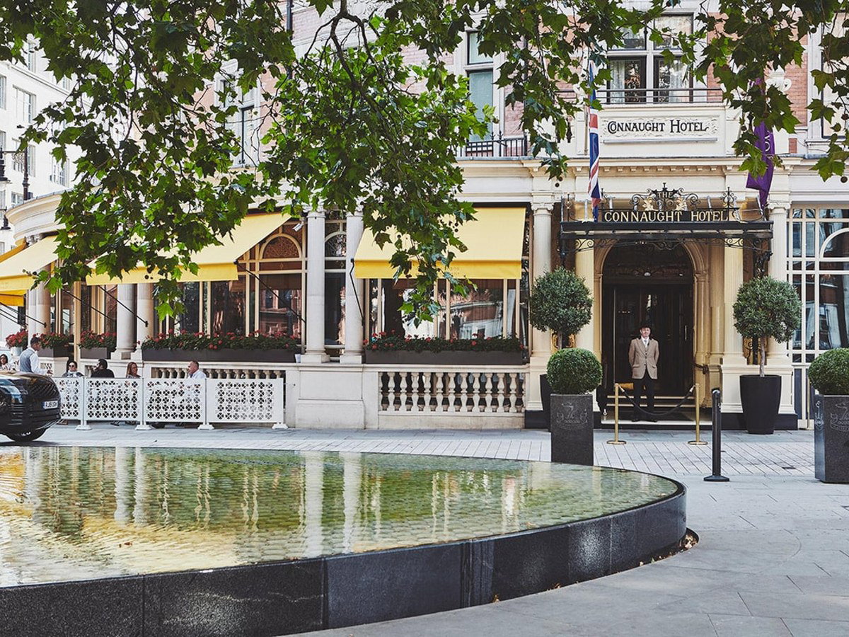 The Connaught Hotel's grand entrance, with its doorman, yellow awnings, and topiary, welcomes guests to Connaught Bar.