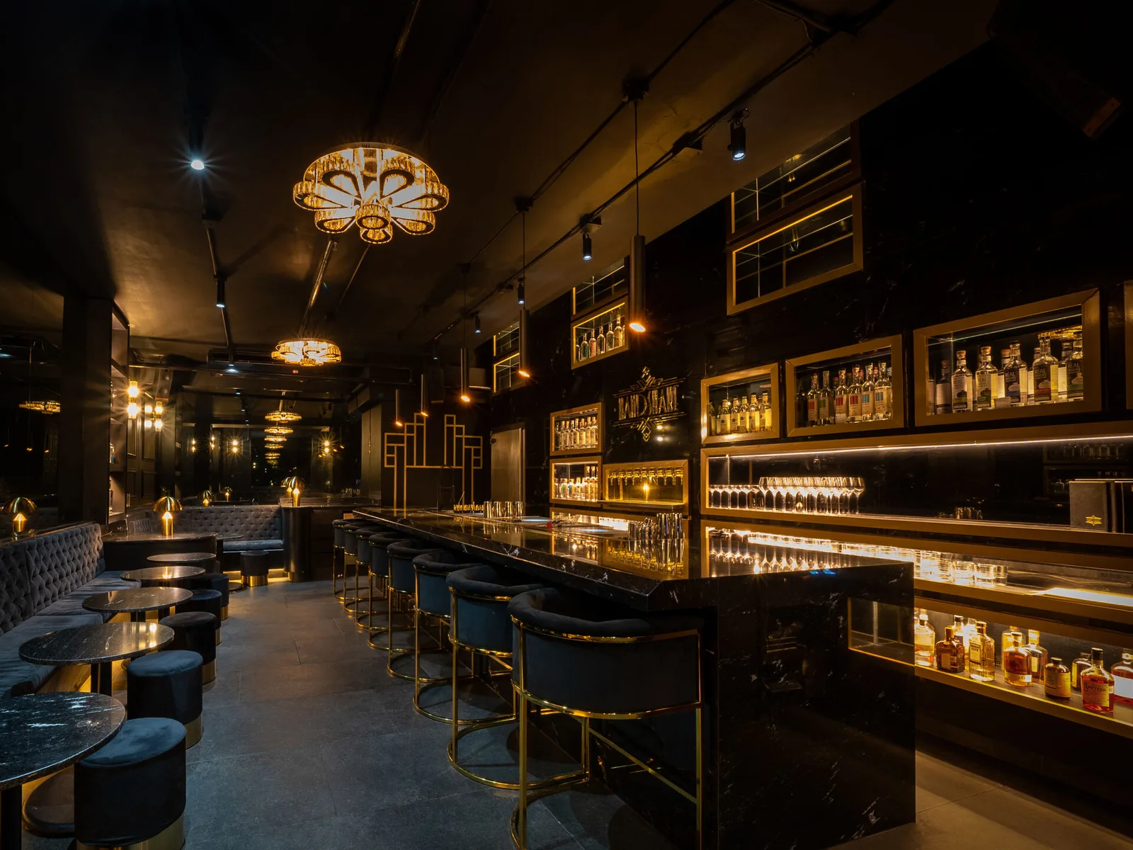 A dimly lit, luxurious bar interior with a long, dark marble counter, high stools, and shelves of liquor bottles.