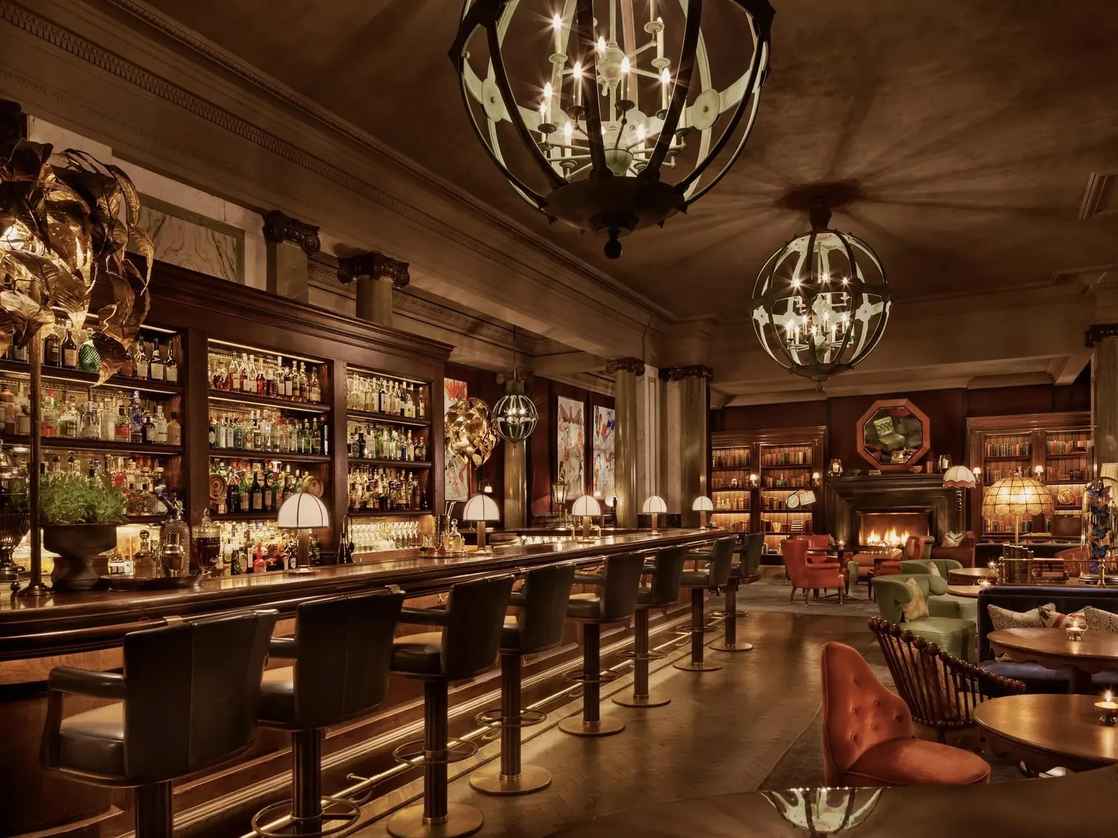 A luxurious bar lounge with dark wood paneling, a lengthy bar counter with black chairs, backlit bottle displays, spherical pendant lights, and comfortable seating areas with warm ambient lighting.
