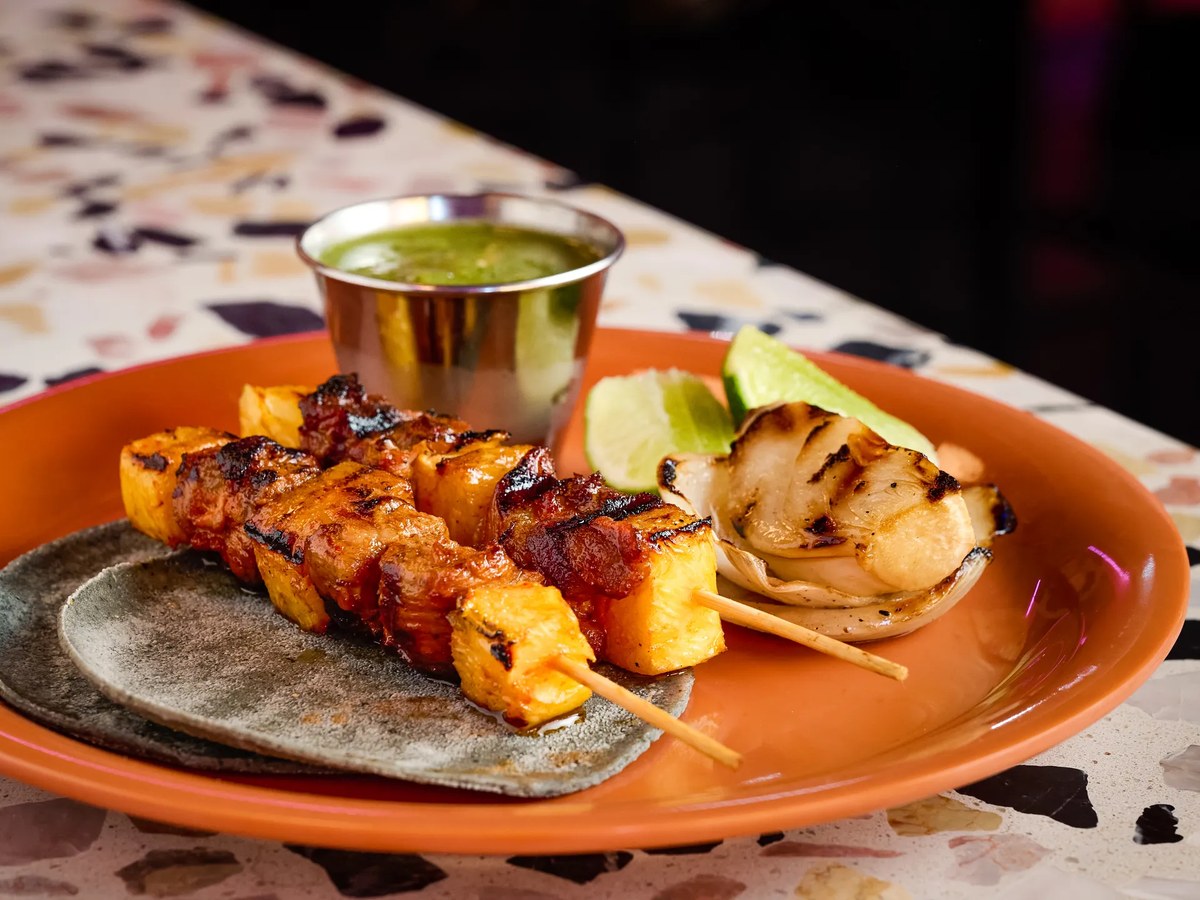 Al Pastor Yaki Tacos from Superbueno's food menu, served with grilled onion, lime, and green sauce.