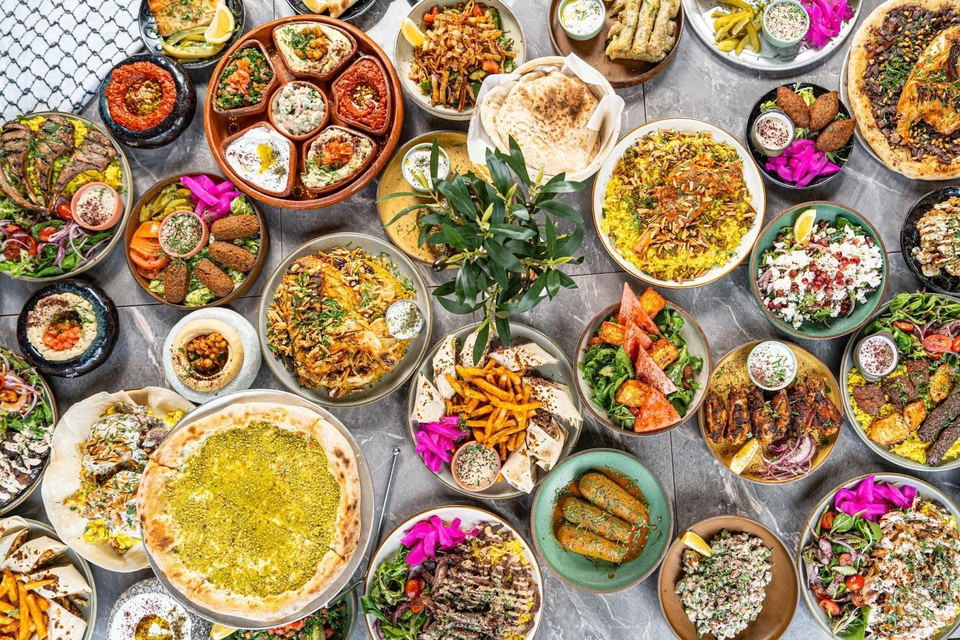 An overhead spread of numerous Middle Eastern and Mediterranean dishes including hummus, falafel, biryani, flatbreads, salads, and grilled meats arran